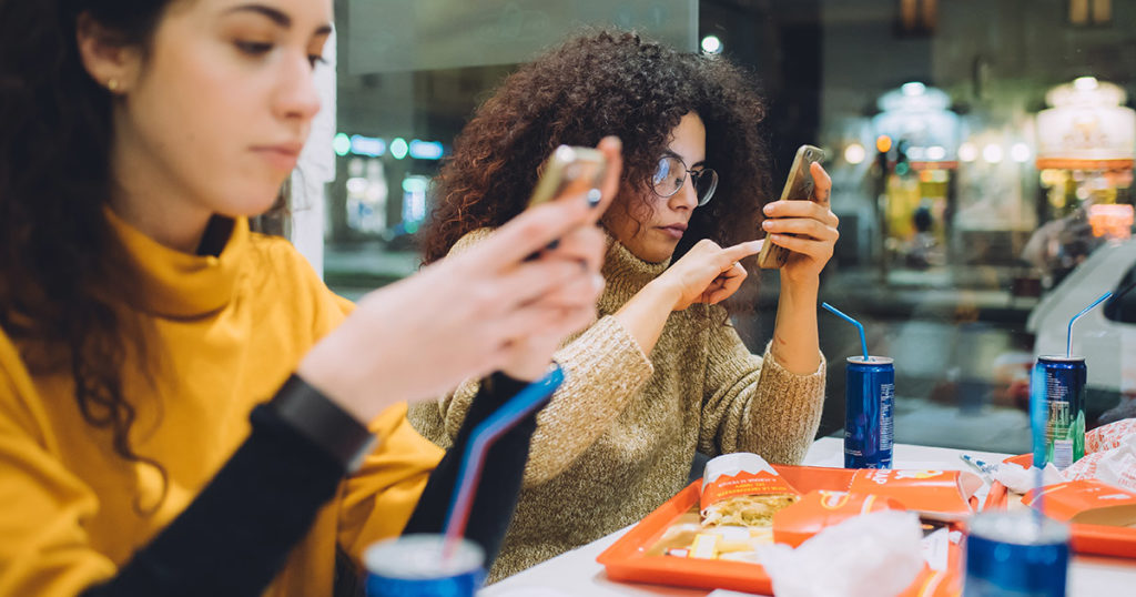 millennials on mobile phone at eating fast food at QSR