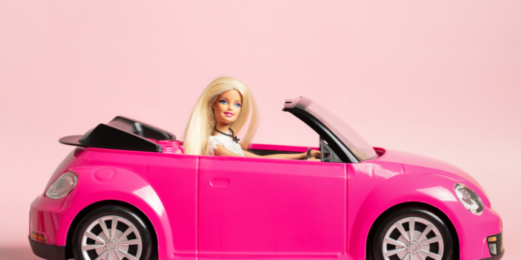 A blonde Barbie doll driving a toy, pink convertible.